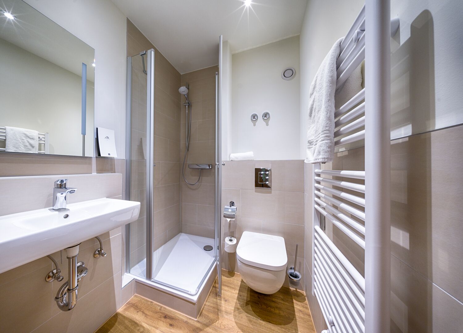 A modern bathroom with a glass-enclosed shower, a white sink, a toilet, and a towel rack.