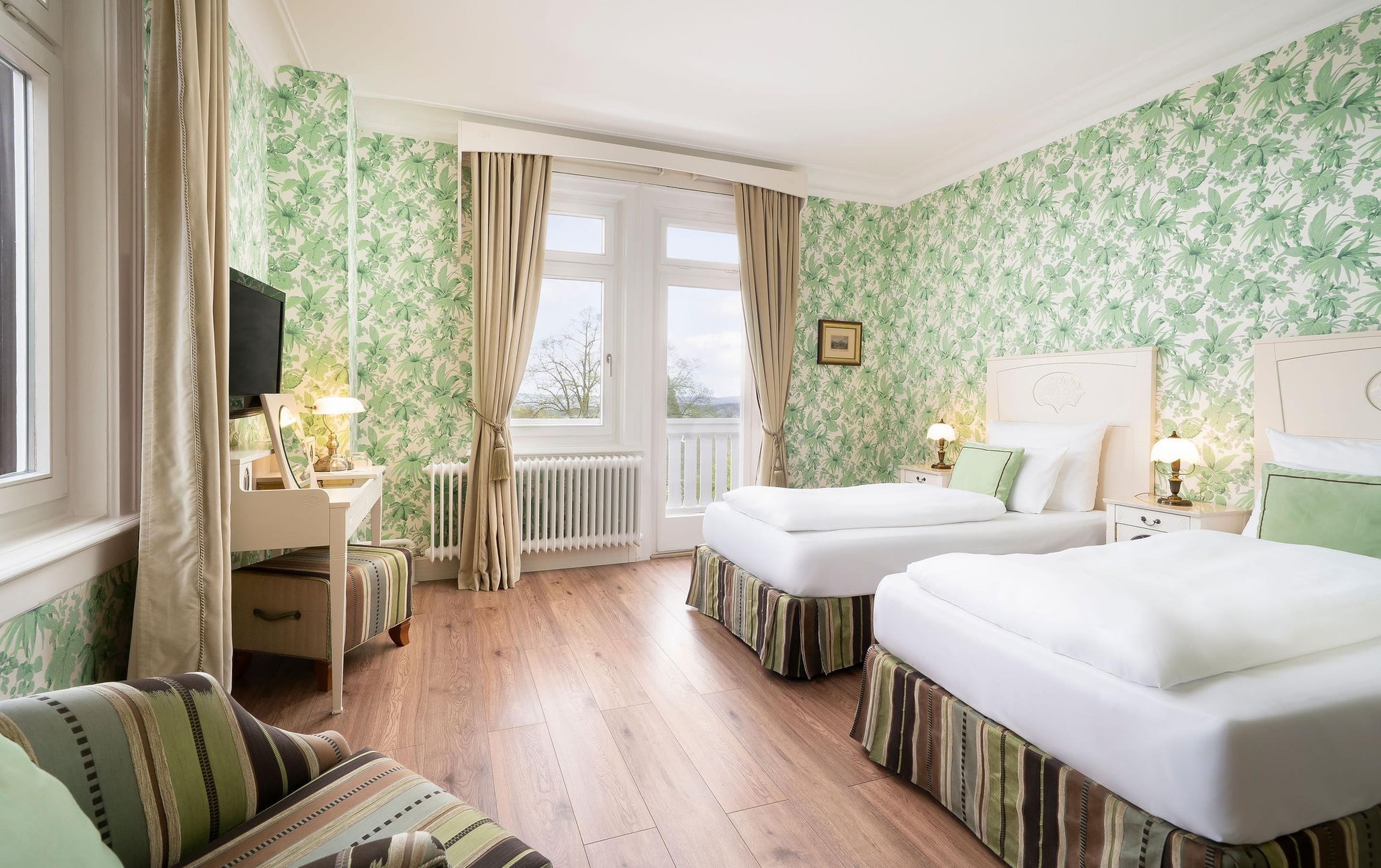 A hotel room with two beds, a sofa, a TV, and a window with curtains.