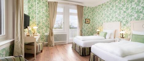 A hotel room with two beds, a sofa, a TV, and a window with curtains.
