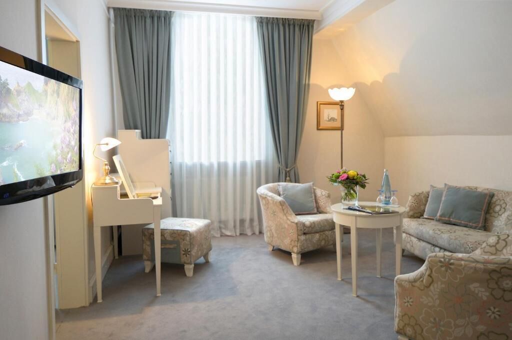 A hotel room with a TV, a desk, a chair, a sofa, and a lamp.