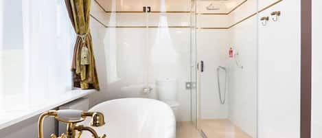 A modern bathroom with a glass-enclosed shower, a white bathtub, and a gold faucet.