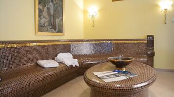 A room with a mosaic-patterned sofa, a round table with a bowl and magazines, and a painting on the wall.