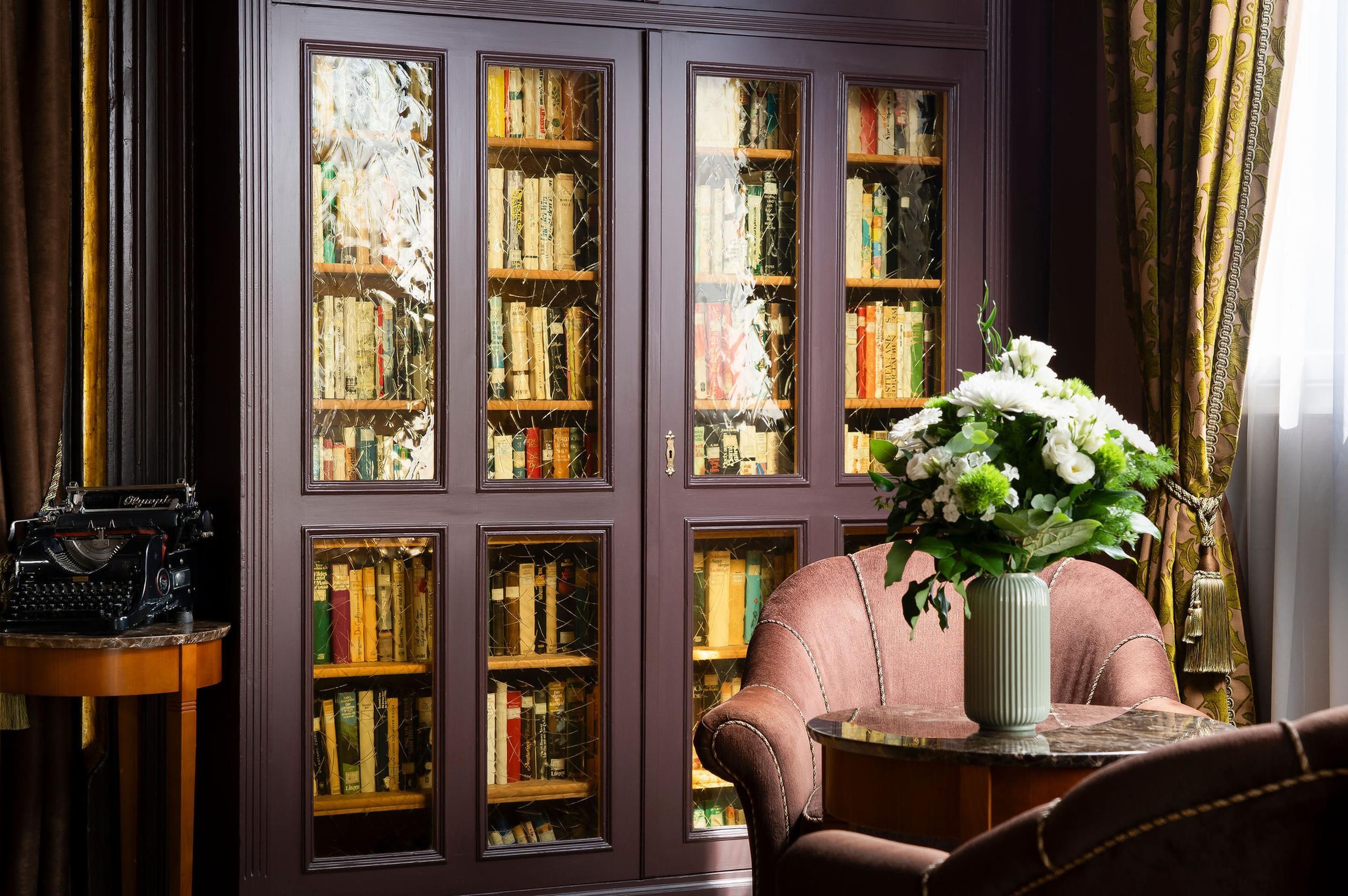 Une bibliothèque avec des étagères remplies de livres, une machine à écrire ancienne et un vase de fleurs.