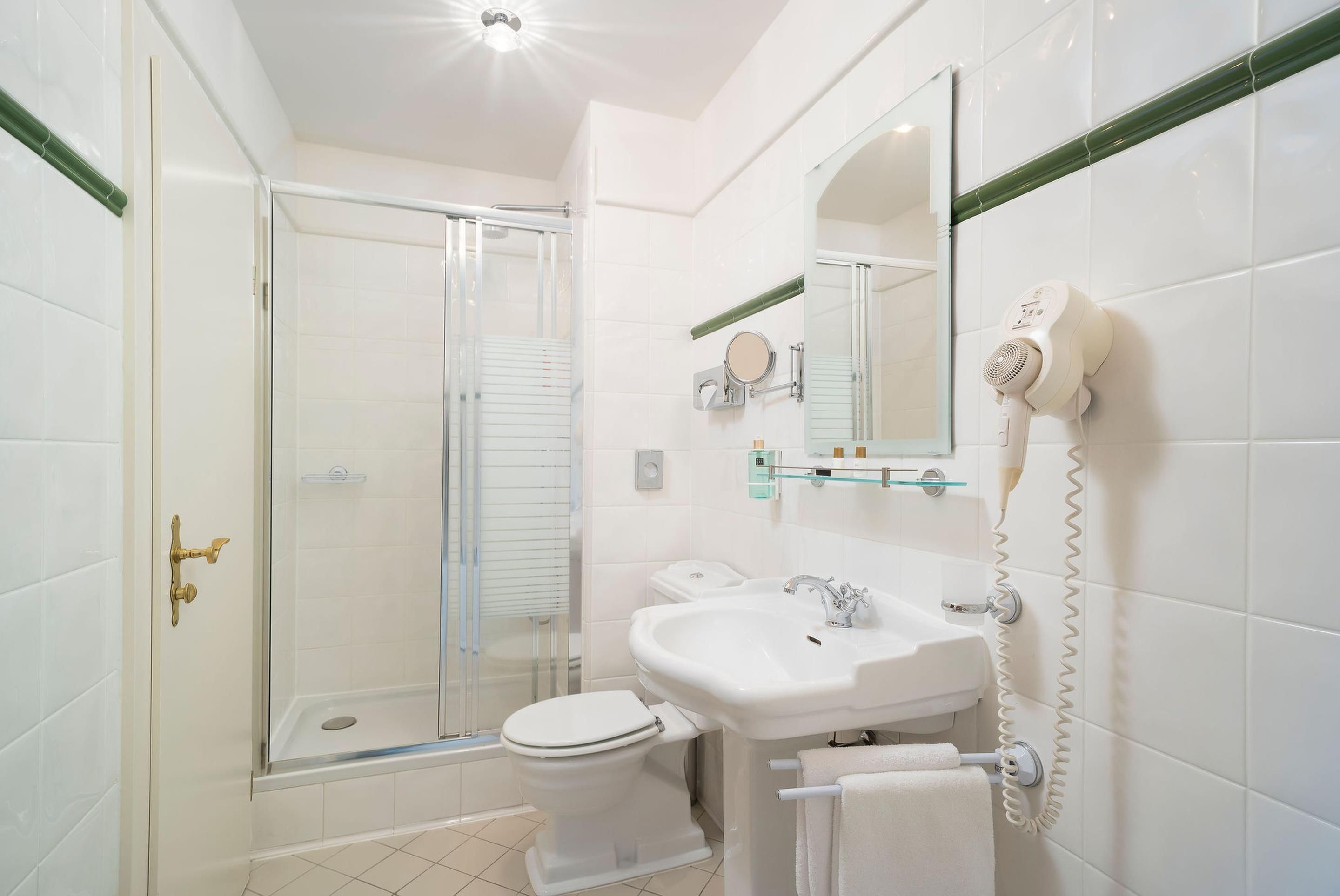 Een moderne badkamer met een douchecabine van glas, een witte wastafel en een haardroger bevestigd aan de muur.