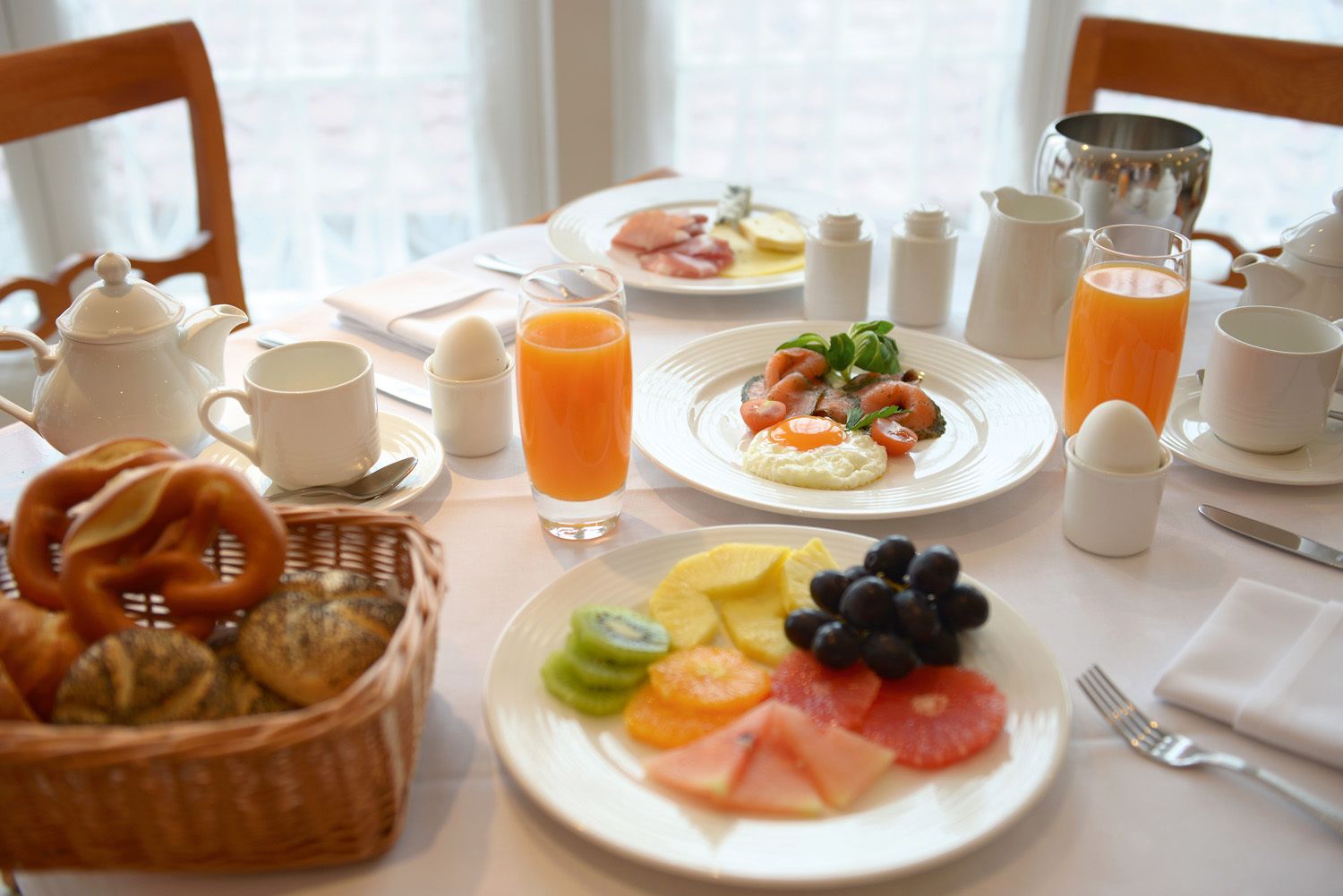 Desayuno con platos de comida, una cesta de pretzels y una jarra de jugo de naranja.