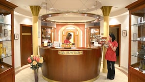 A reception desk labeled "SPA RECEPTION" with a woman standing beside it, a vase of flowers, and a display of fruits. - Das Palmenwald Schwarzwaldhof, BW Signature Collection (Freudenstadt)