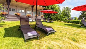 A patio area with two reclining chairs, each under a red umbrella, and a building with a porch in the background. - Das Palmenwald Schwarzwaldhof, BW Signature Collection (Freudenstadt)