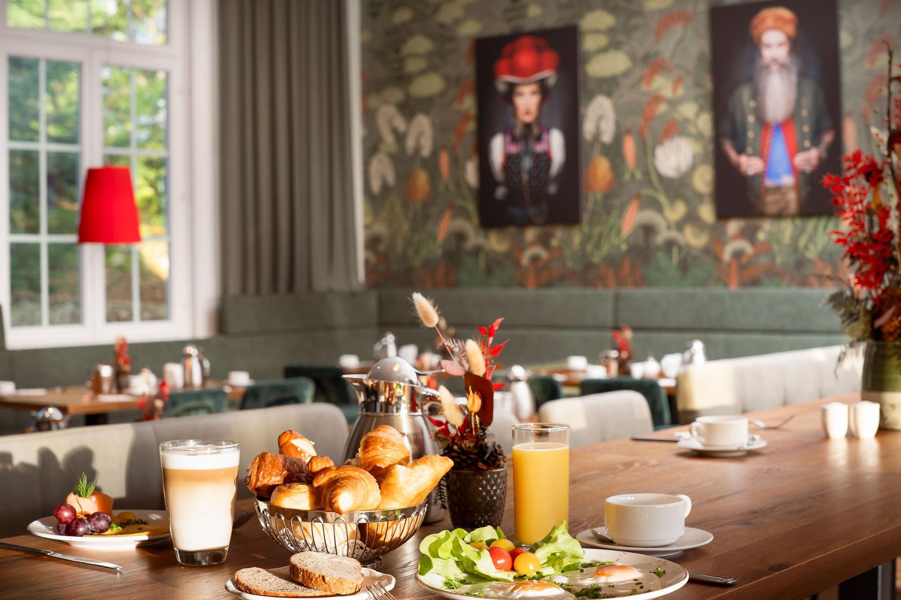 A breakfast setting with croissants, a fruit bowl, a glass of milk, and a juice pitcher on a wooden table.