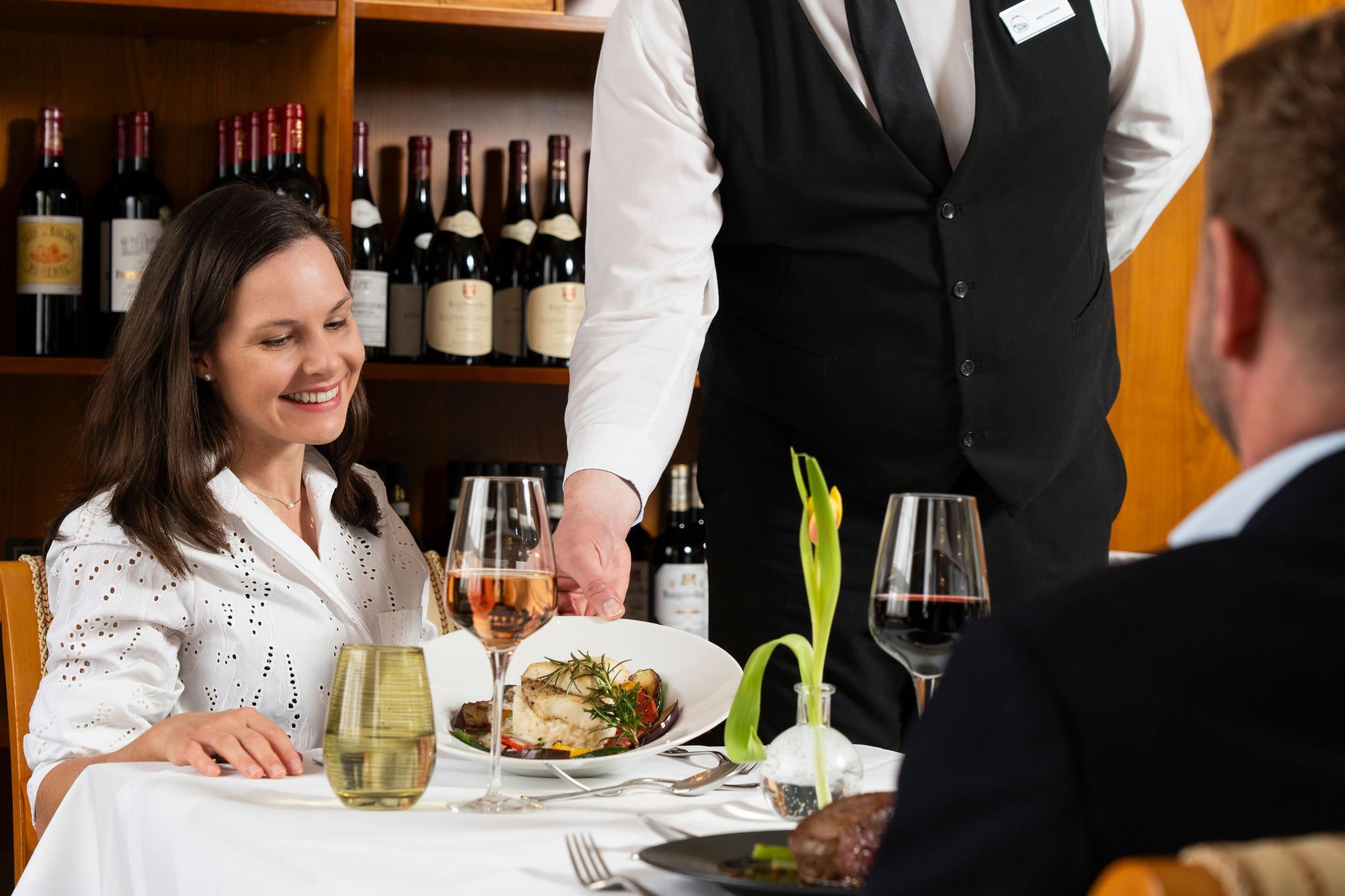 A dining table with a plate of food, a wine glass, and a bottle of wine.