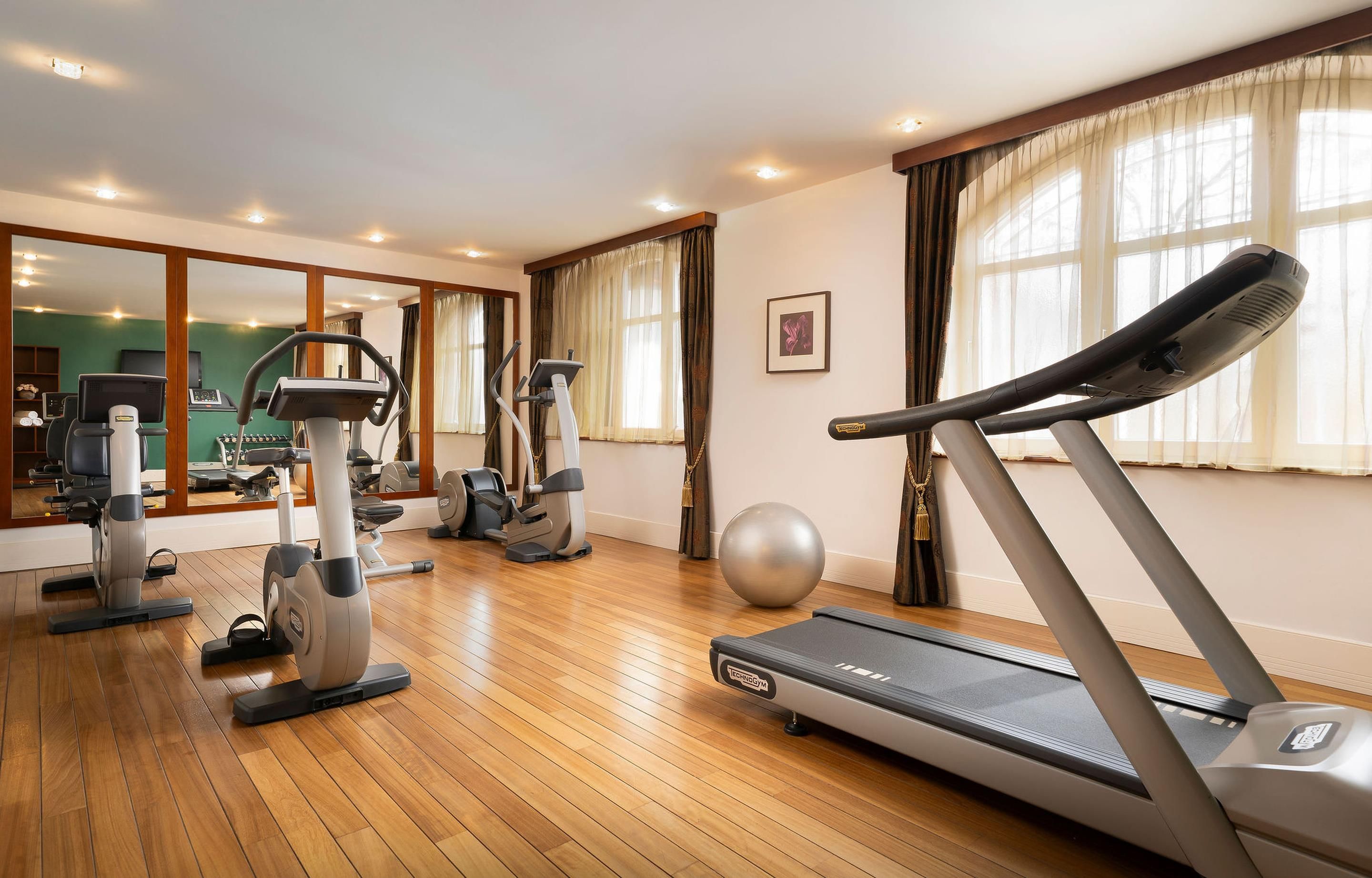 A gym with cardio machines, a mirrored wall, and large windows.