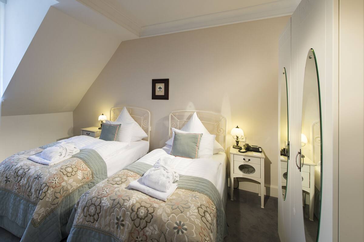 A bedroom with two beds, a small bedside table with a lamp, and a mirror on the wall.