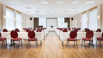 A conference room with rows of tables and chairs, a large screen at the front, and a wooden floor.