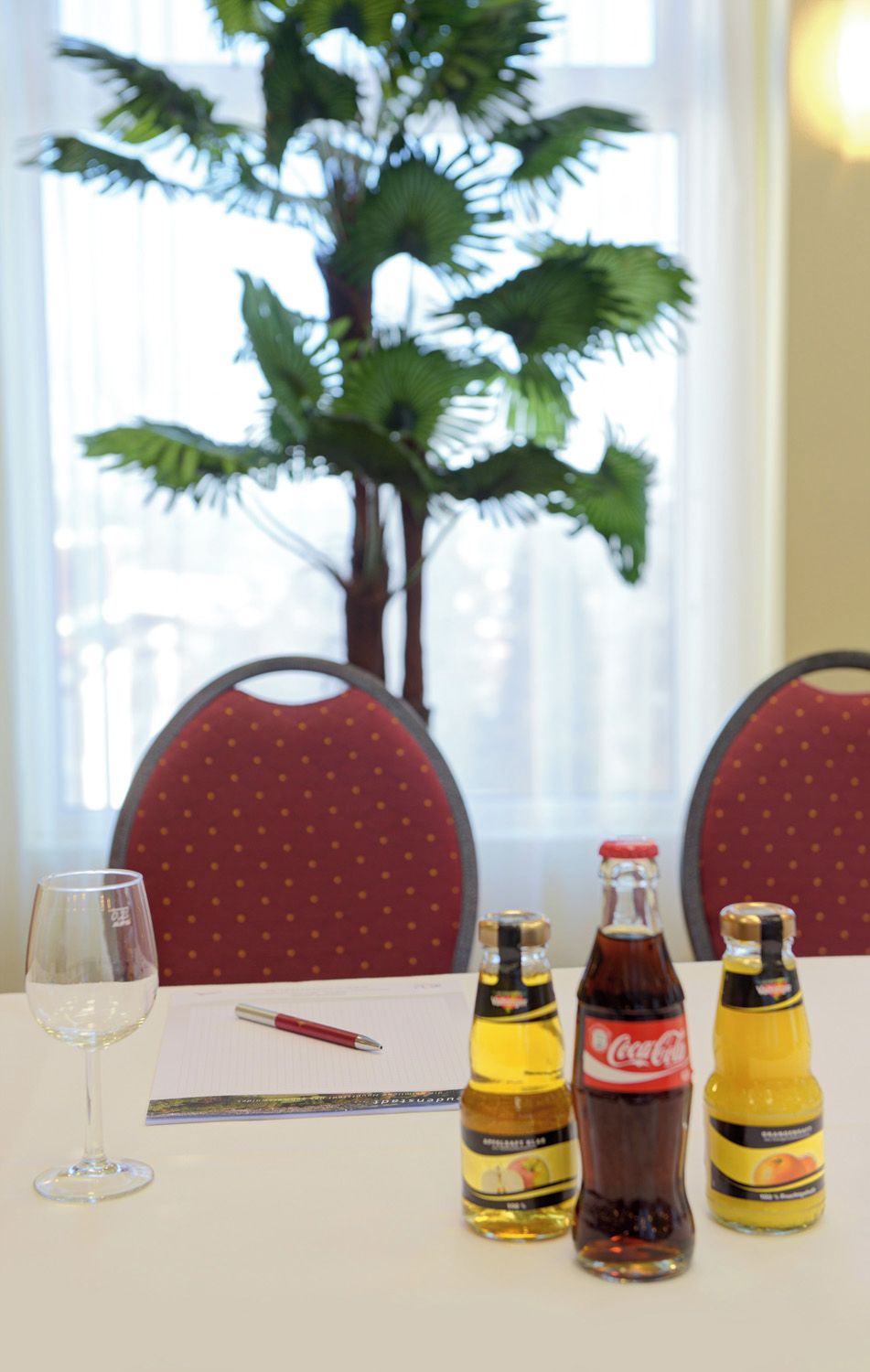 A table with a glass of white wine, a pen, and three bottles of beverages.