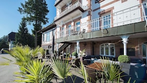 A building with a balcony, outdoor seating, and potted plants. - Das Palmenwald Schwarzwaldhof, BW Signature Collection (Freudenstadt)