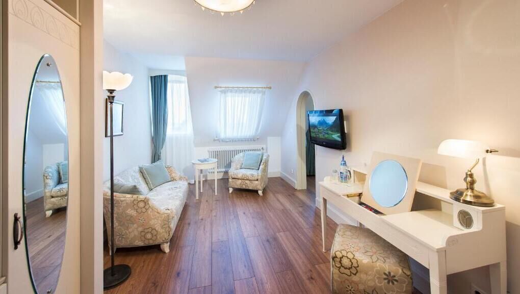 Une chambre d’hôtel avec un plancher en bois, un canapé, une chaise, une petite table, un téléviseur et un bureau avec une lampe.