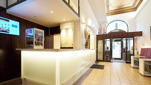 Un espace d’accueil d’hôtel au design moderne, avec un comptoir d’accueil, un écran numérique et une vue sur l’entrée.
