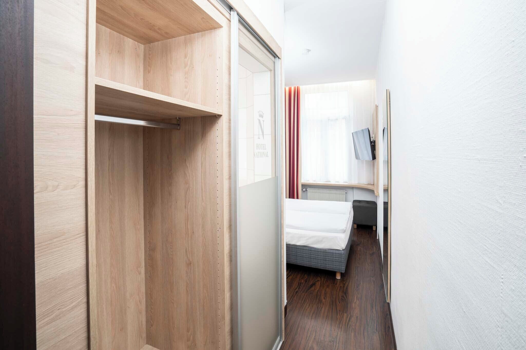 Une chambre d’hôtel avec une armoire en bois, un lit, un radiateur et un téléviseur fixé au mur.