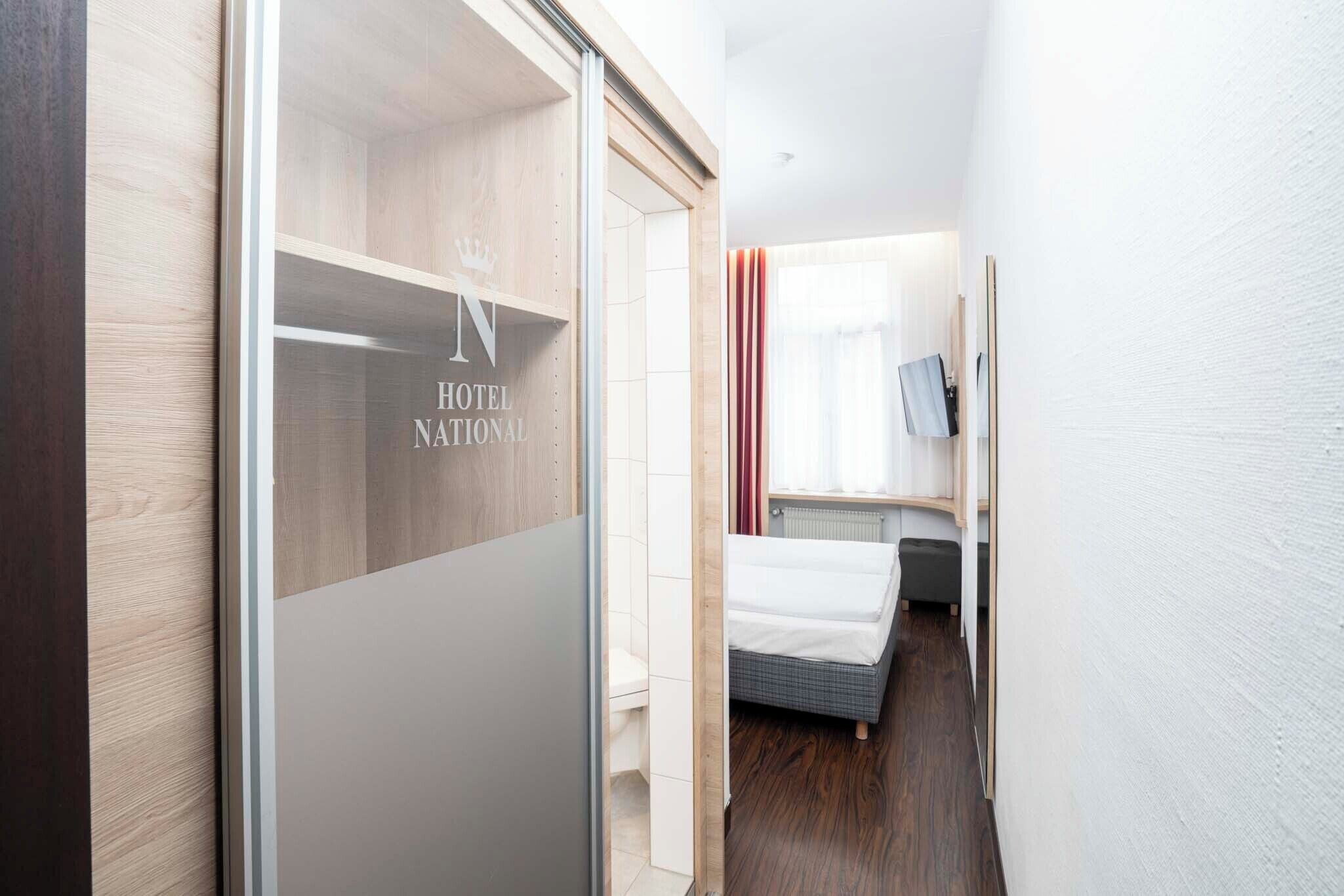 Una habitación de hotel con cama, mesita de noche, espejo y ventana con cortinas.