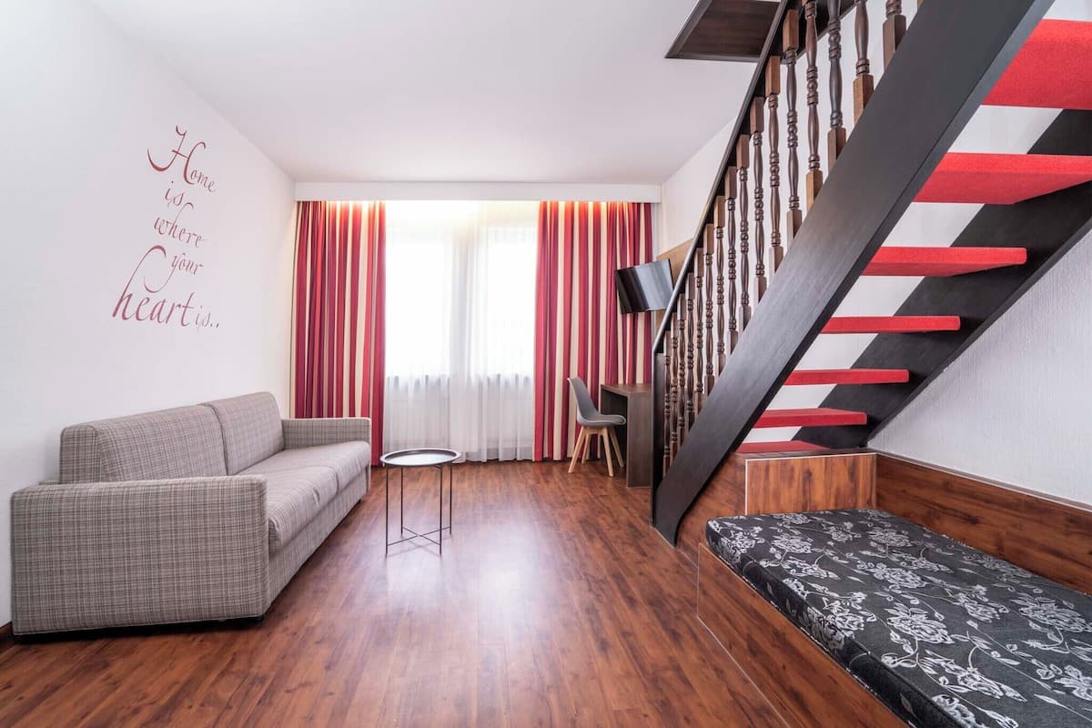 A modern living room with a sofa, a small round table, and a bench. There is a staircase with red and black steps.