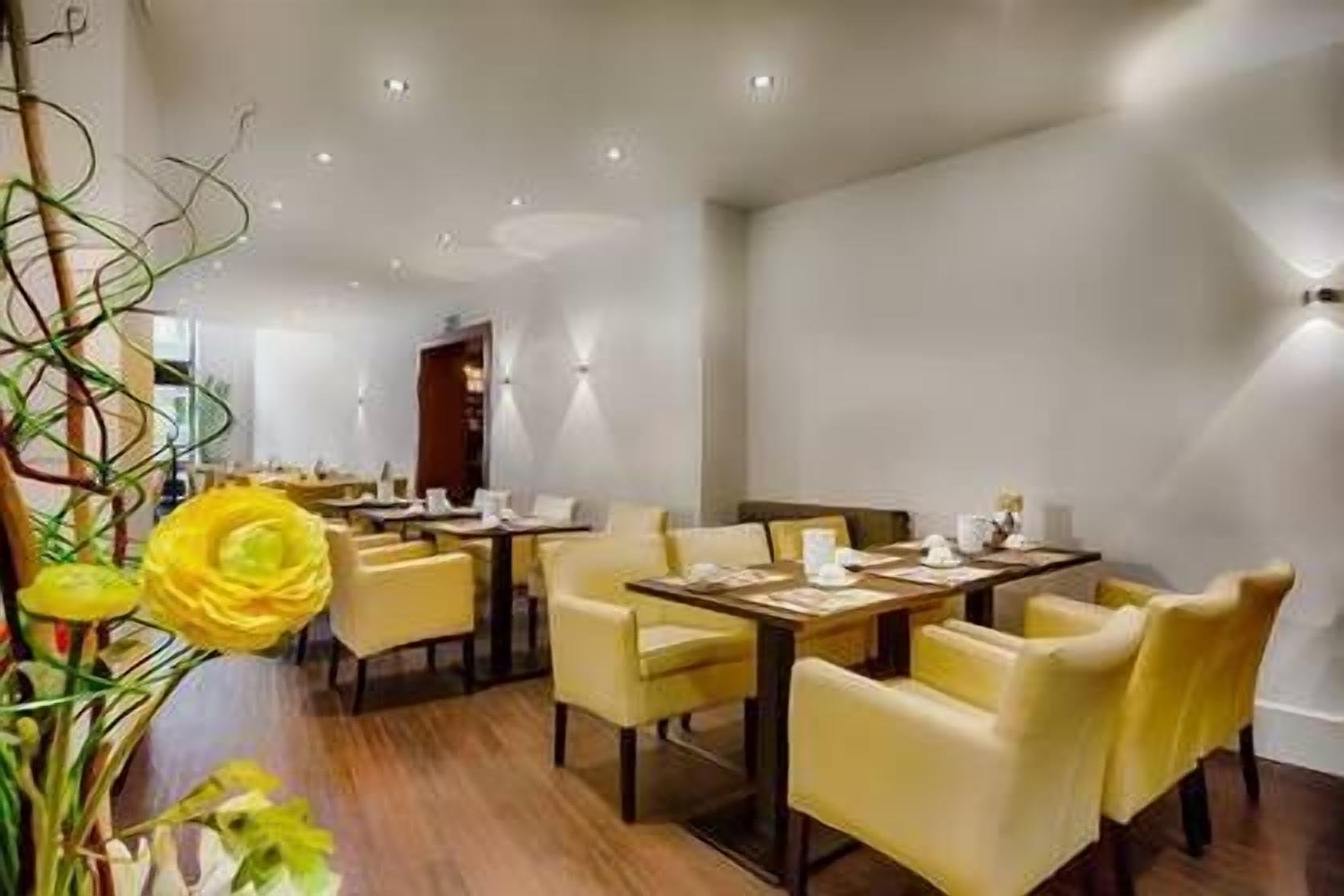 A modern dining area with yellow chairs and tables, a wooden floor, and a large yellow flower in the foreground.