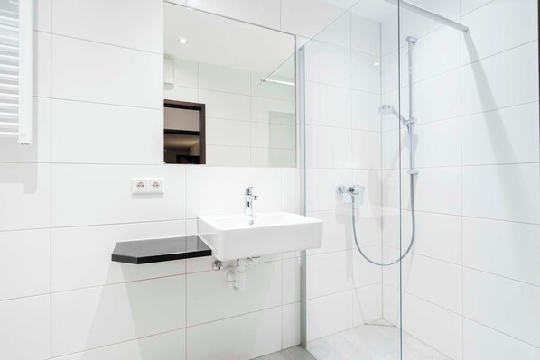 Un baño moderno con lavamanos blanco, espejo y cabina de ducha con paredes de vidrio.