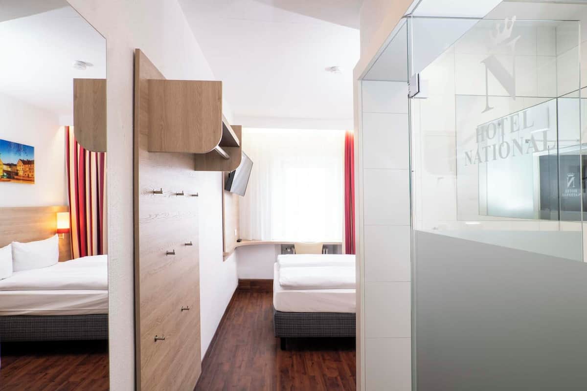 A hotel room with two beds, a wooden wardrobe, a TV, and a window with curtains.