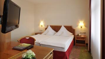 Quarto de hotel com cama, mesas de cabeceira, escrivaninha com luminária, televisão e um vaso de flores.