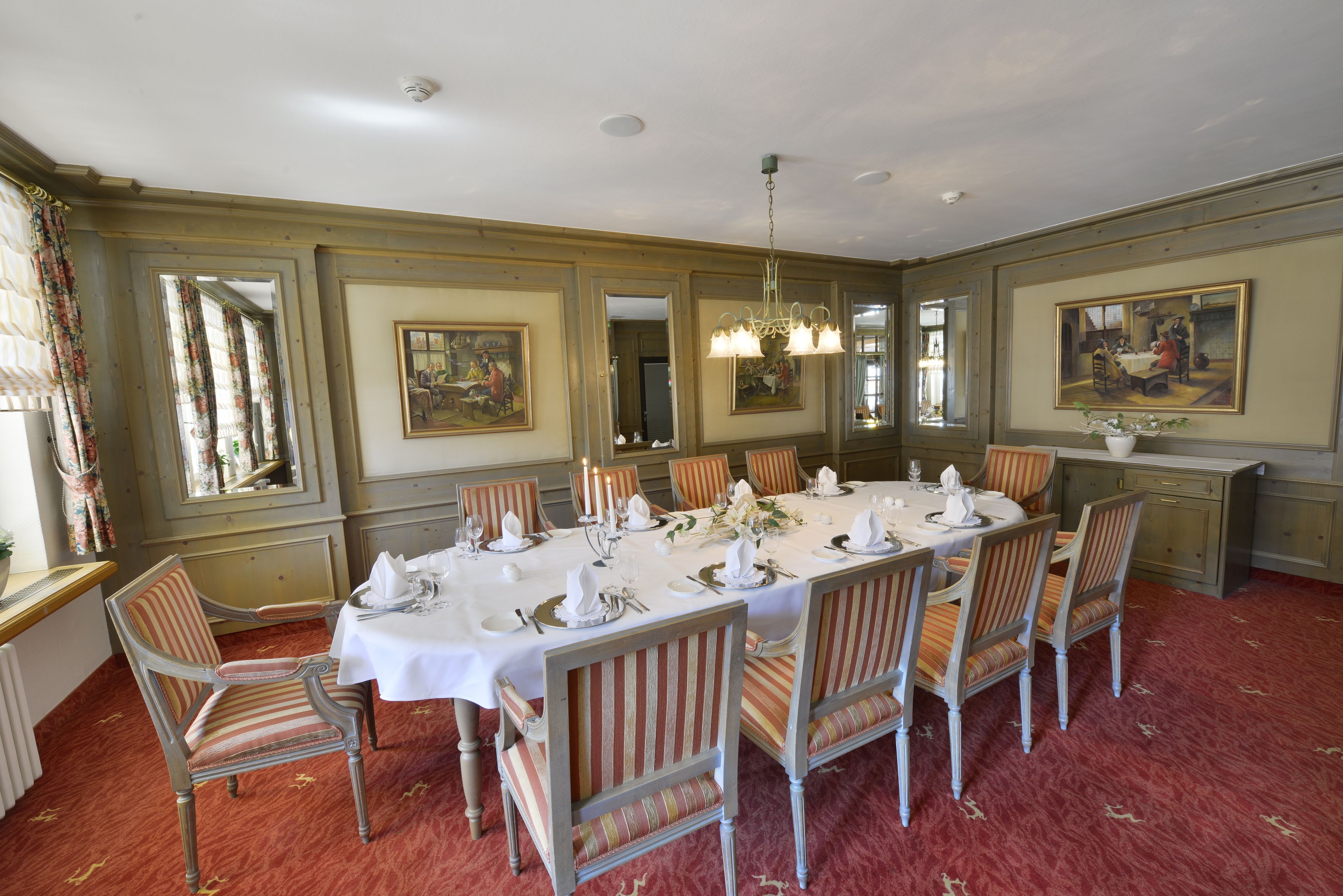 Un comedor formal con una larga mesa dispuesta para una comida, rodeada de sillas y decorada con cuadros y una araña.