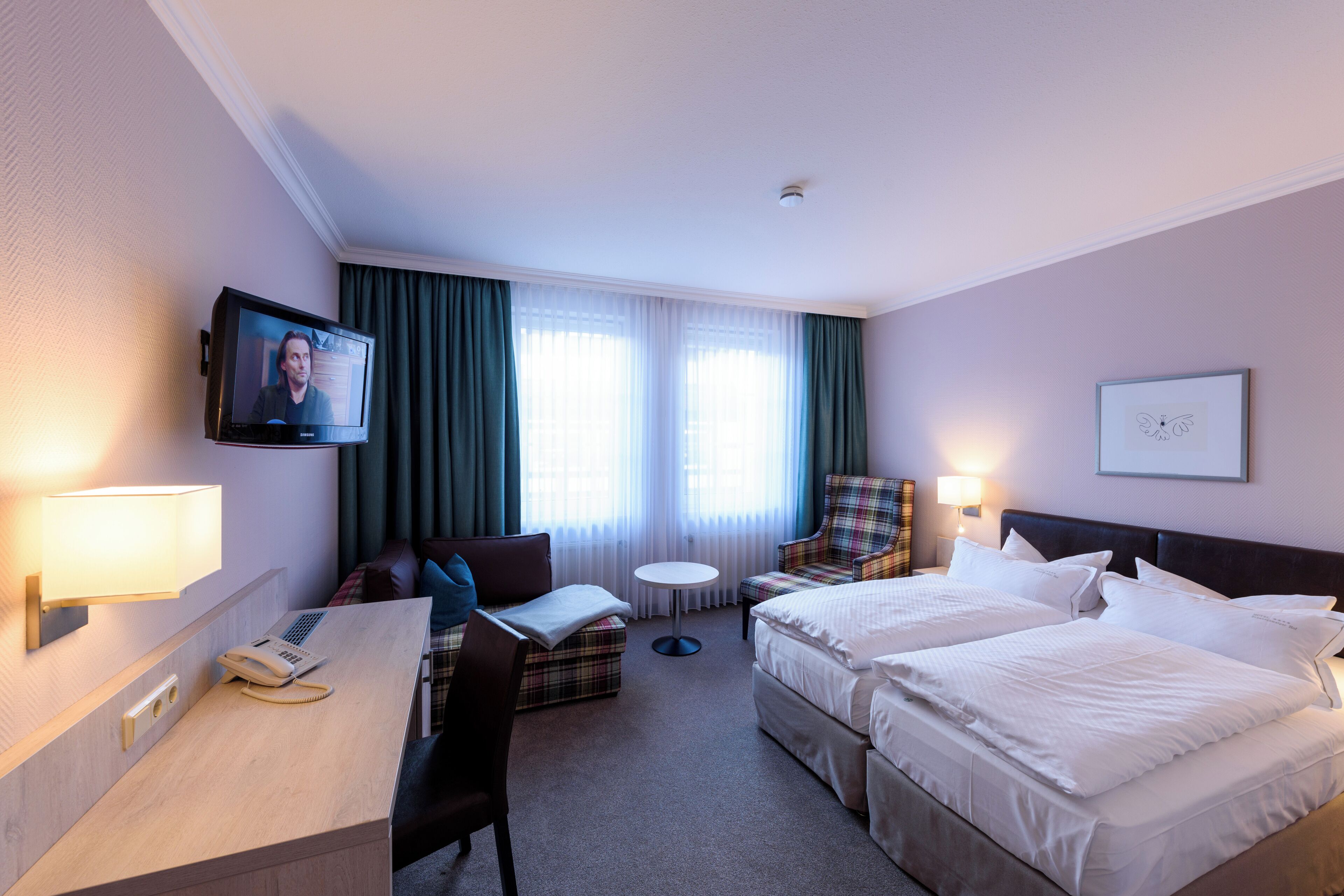 A hotel room with two beds, a desk with a telephone, a chair, a small round table, and a television mounted on the wall.