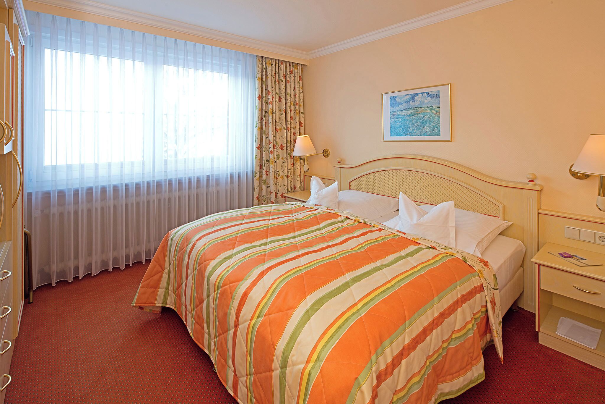 A hotel room with a large bed, a nightstand, a lamp, a painting on the wall, and a window with curtains.