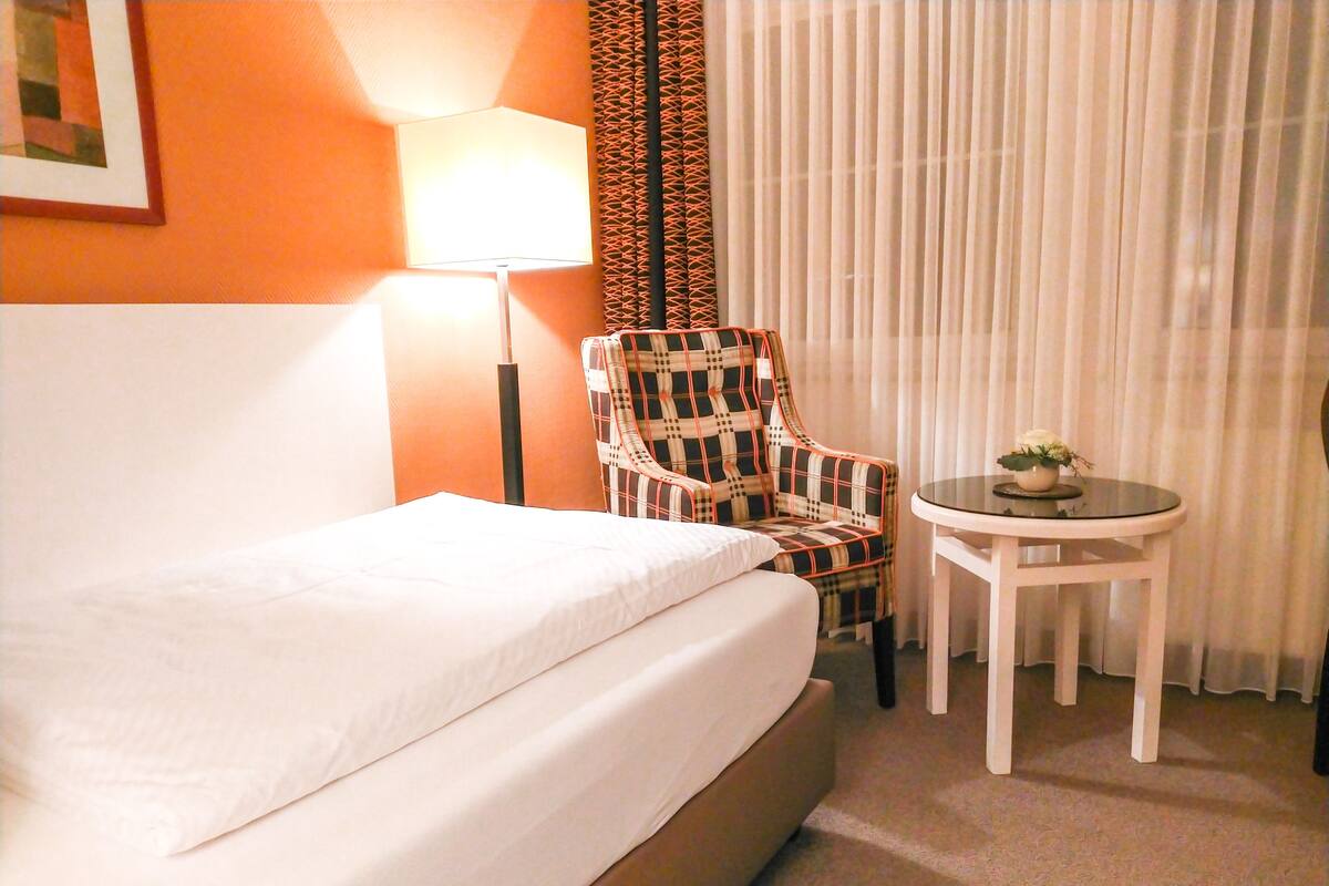 A hotel room with a bed, a chair, a table, and a lamp.