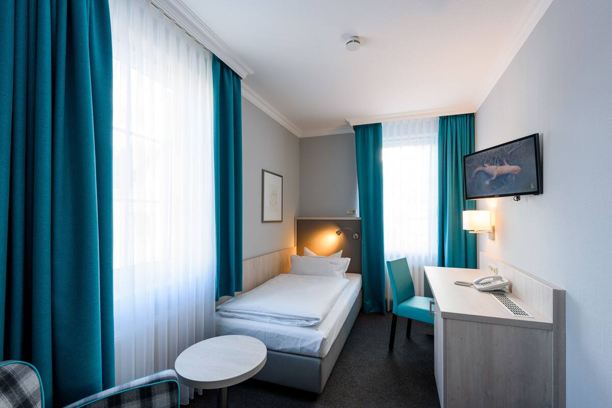 A hotel room with a bed, a desk with a telephone, a chair, and a television on the wall.