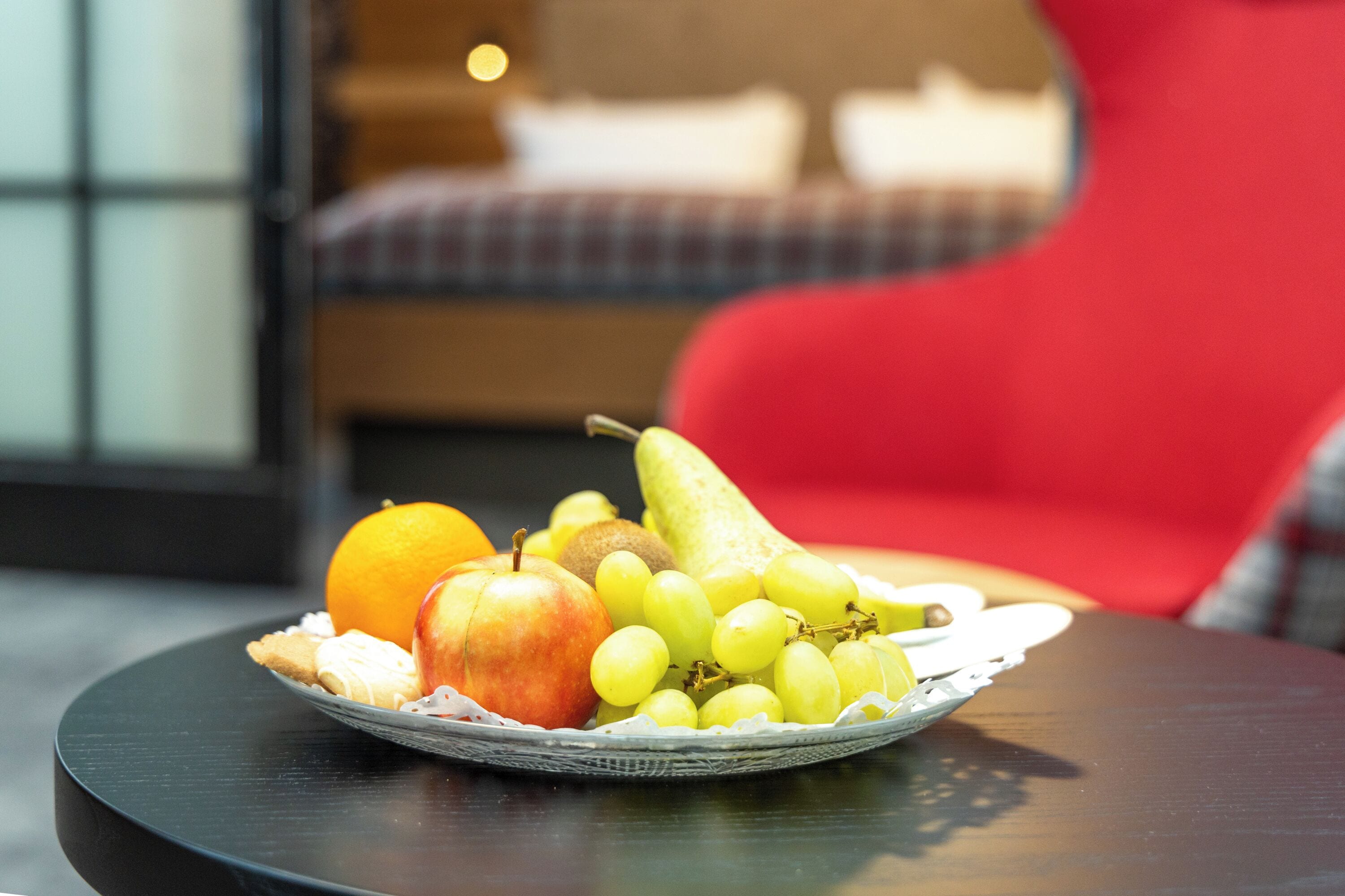 Een fruitschaal op een tafel, met een rode stoel op de achtergrond.