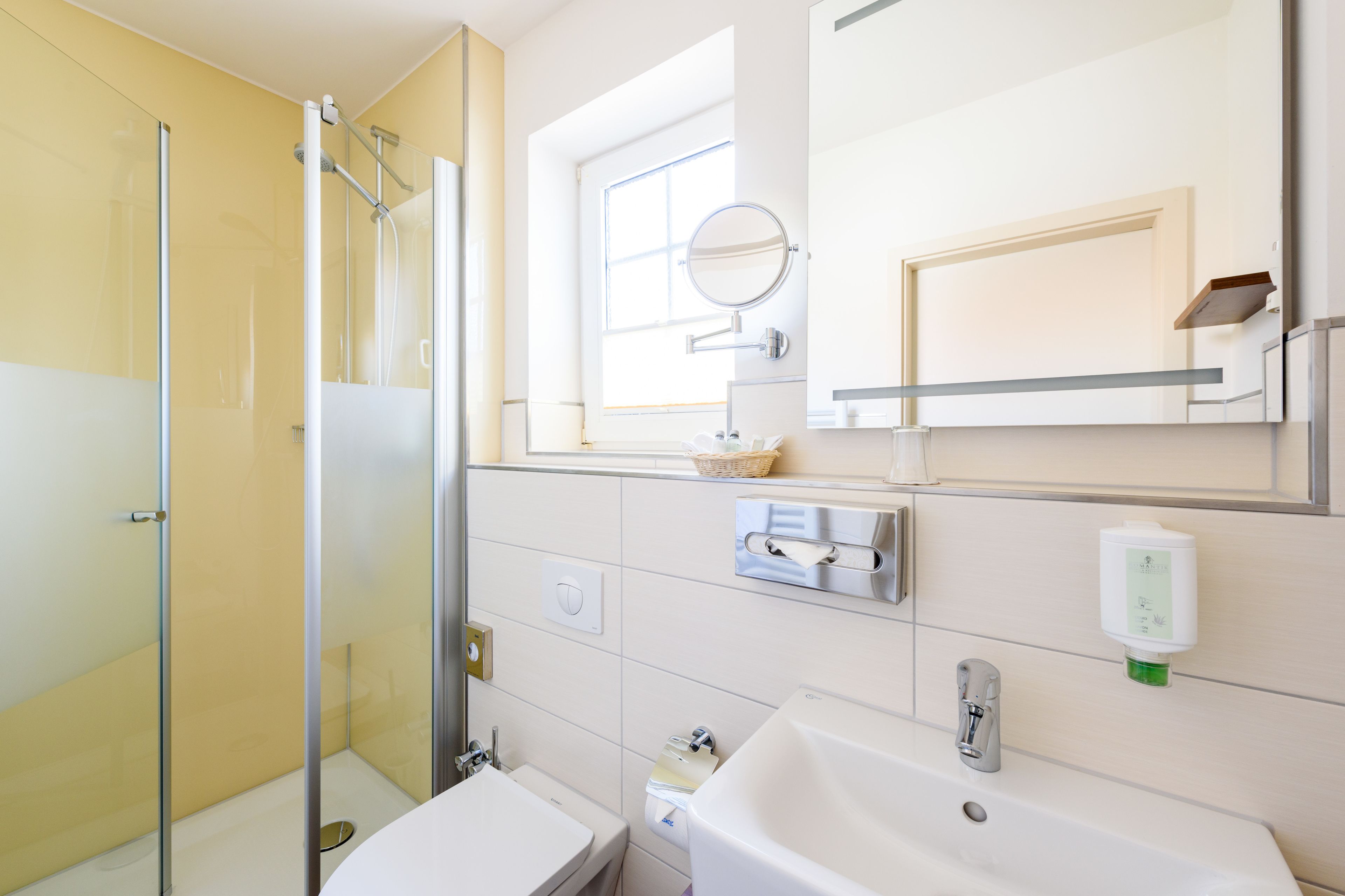 A bathroom with a glass shower enclosure, a sink, a mirror, and a window.