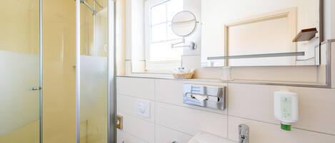 A bathroom with a glass shower enclosure, a sink, a mirror, and a window.