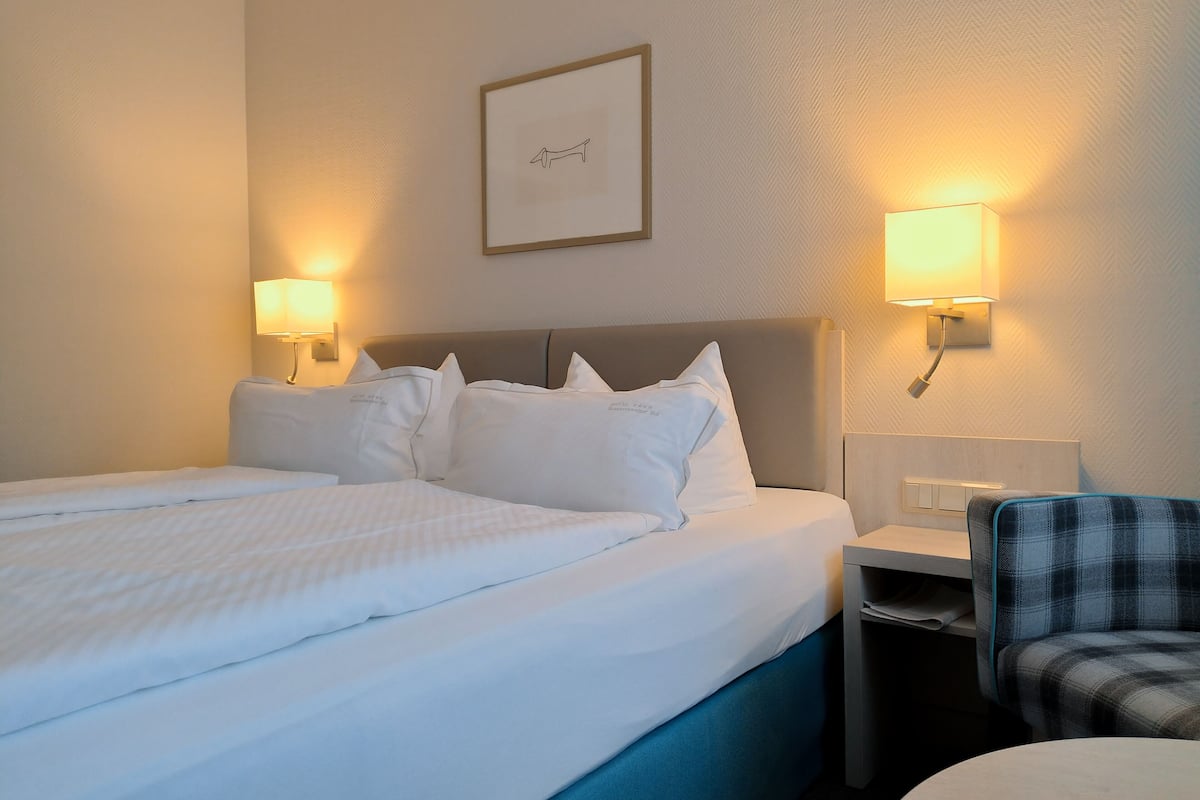 A hotel room with a large bed, two bedside lamps, a framed picture on the wall, and a chair.