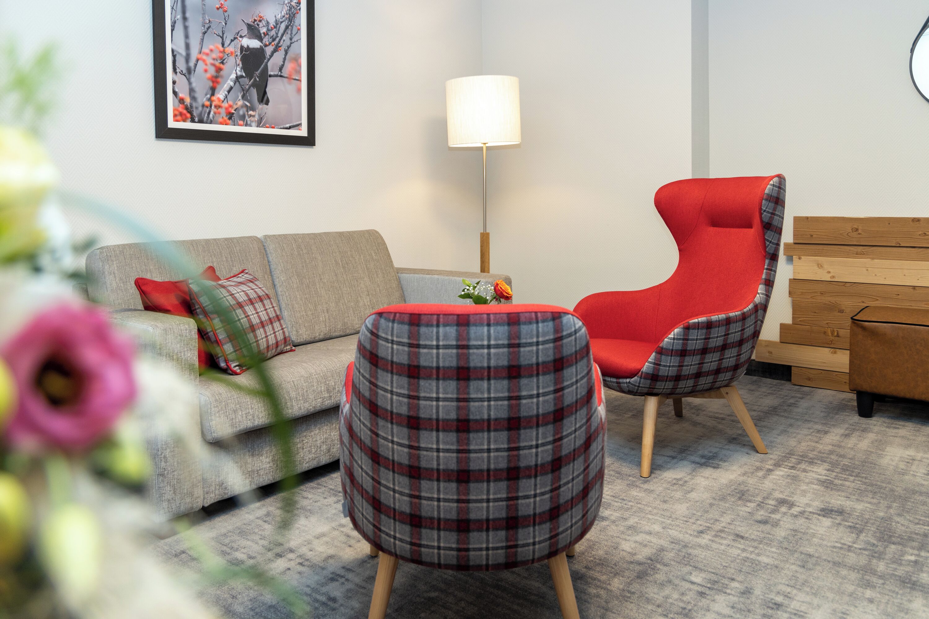 A living room with a grey sofa, a red chair, a plaid ottoman, and a wooden bench.