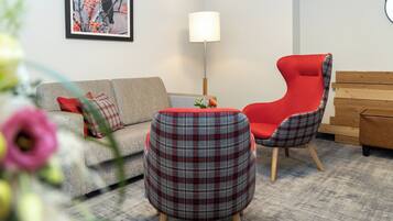 A living room with a grey sofa, a red chair, a plaid ottoman, and a wooden bench.