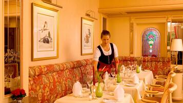 Un área de comedor con un sofá floral rojo, mesas dispuestas con manteles blancos y cuadros en las paredes.