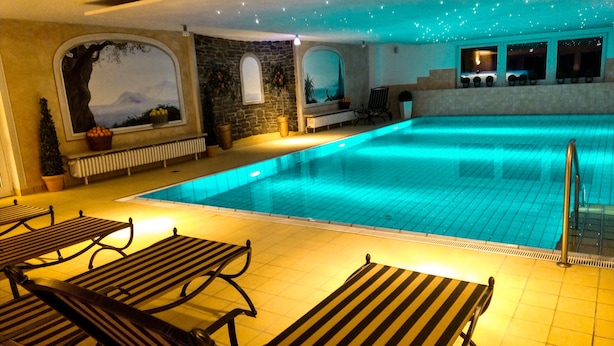 A swimming pool with lounge chairs, a stone wall, and a view of the mountains.