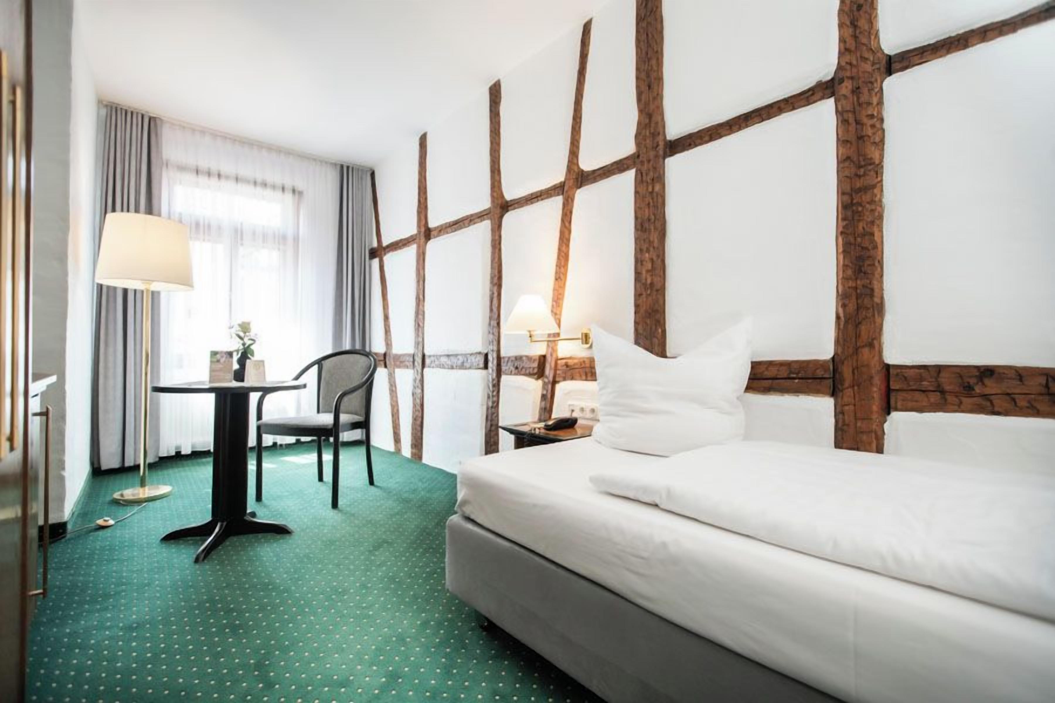 A hotel room with a bed, a desk, a chair, and a lamp.