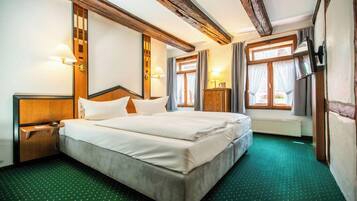 Ein Hotelzimmer mit einem großen Bett, einem Holzkopfteil, zwei Nachttischen, einem Beistelltisch, einem Fenster mit Vorhängen und einem Fernseher.