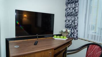 A room with a wooden desk, a television, a remote control, a plate with apples, and a chair.