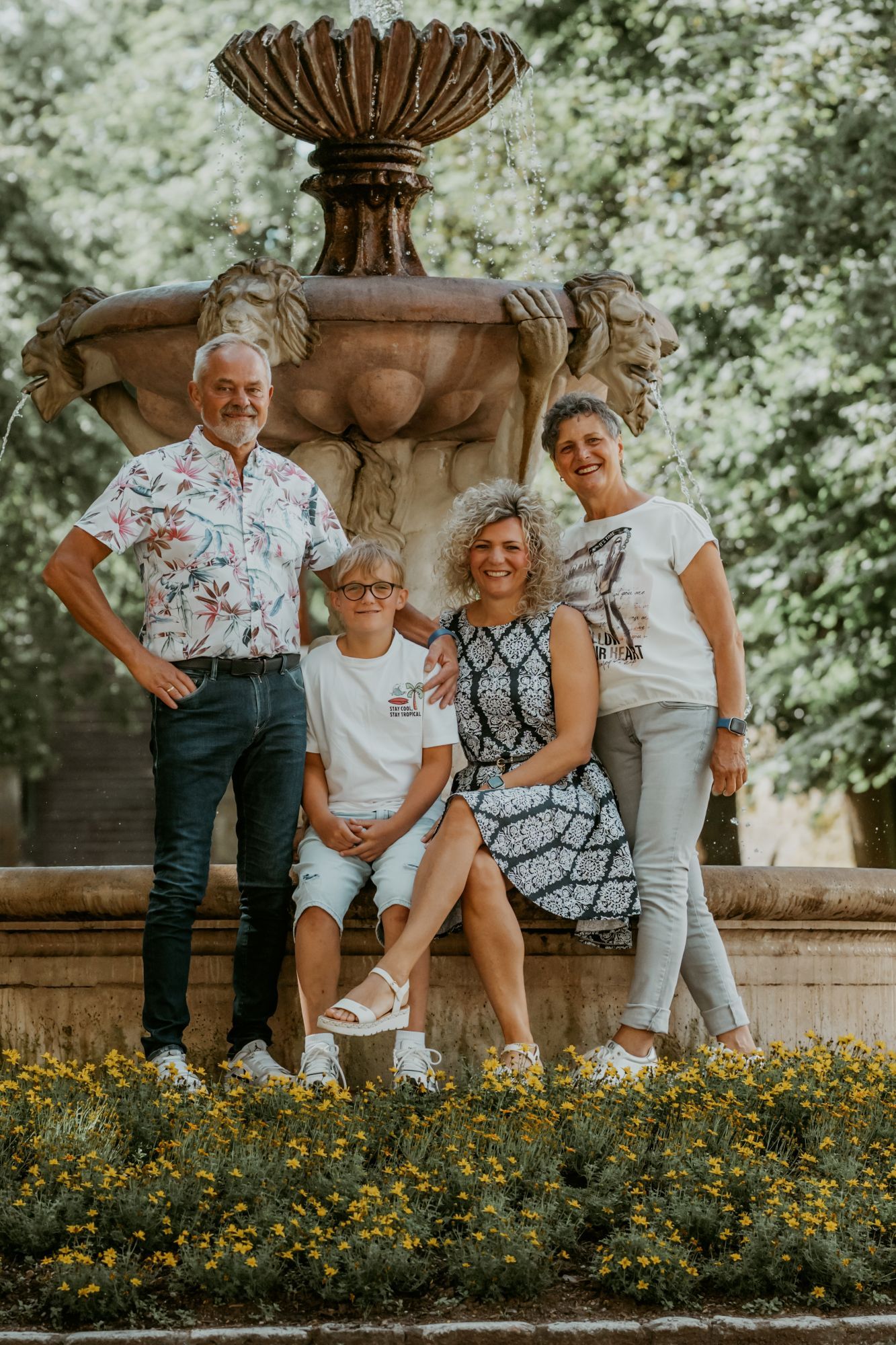 A family of four posing in front of a fountain with a lion statue, surrounded by yellow flowers.