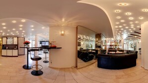 Un'ampia hall con reception, zona bar e salottino con un grande divano nero.