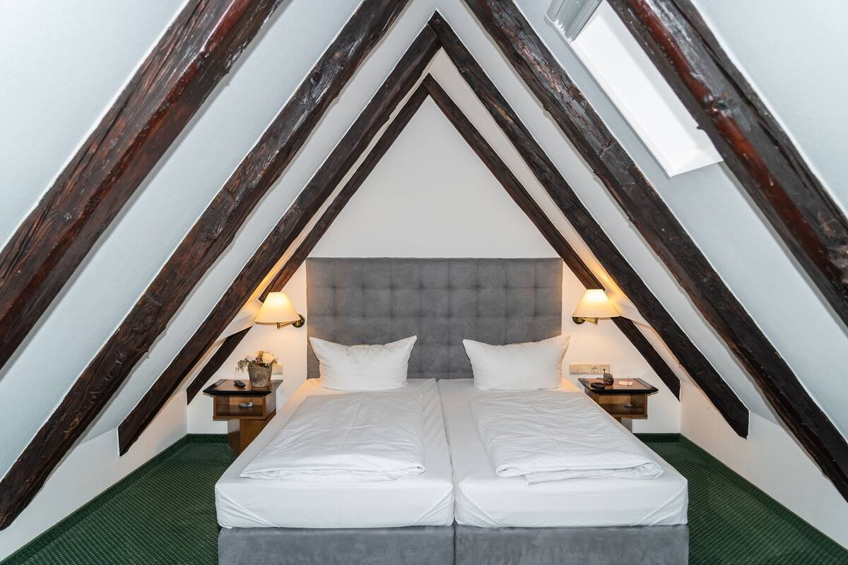 Una habitación con techo abovedado, dos camas, mesitas de noche con lámparas y una alfombra verde.