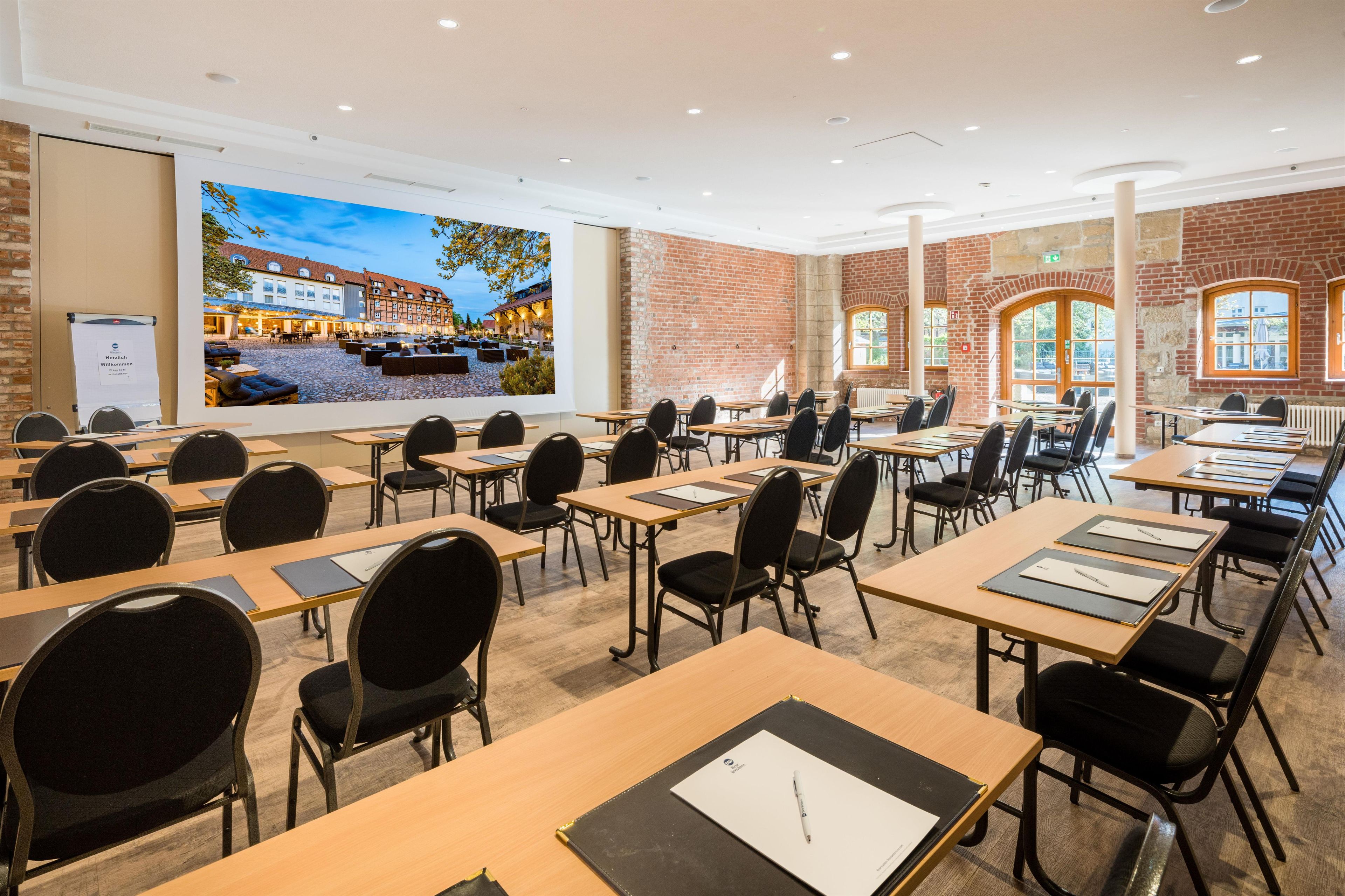 Una sala conferenze con tavoli, sedie, un grande schermo e pareti in mattoni.