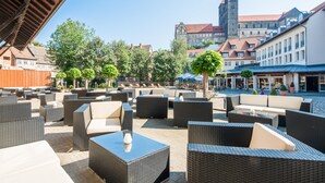 An outdoor seating area with wicker furniture and a view of historic buildings in the background. - Best Western Hotel Schlossmuehle (Quedlinburg)