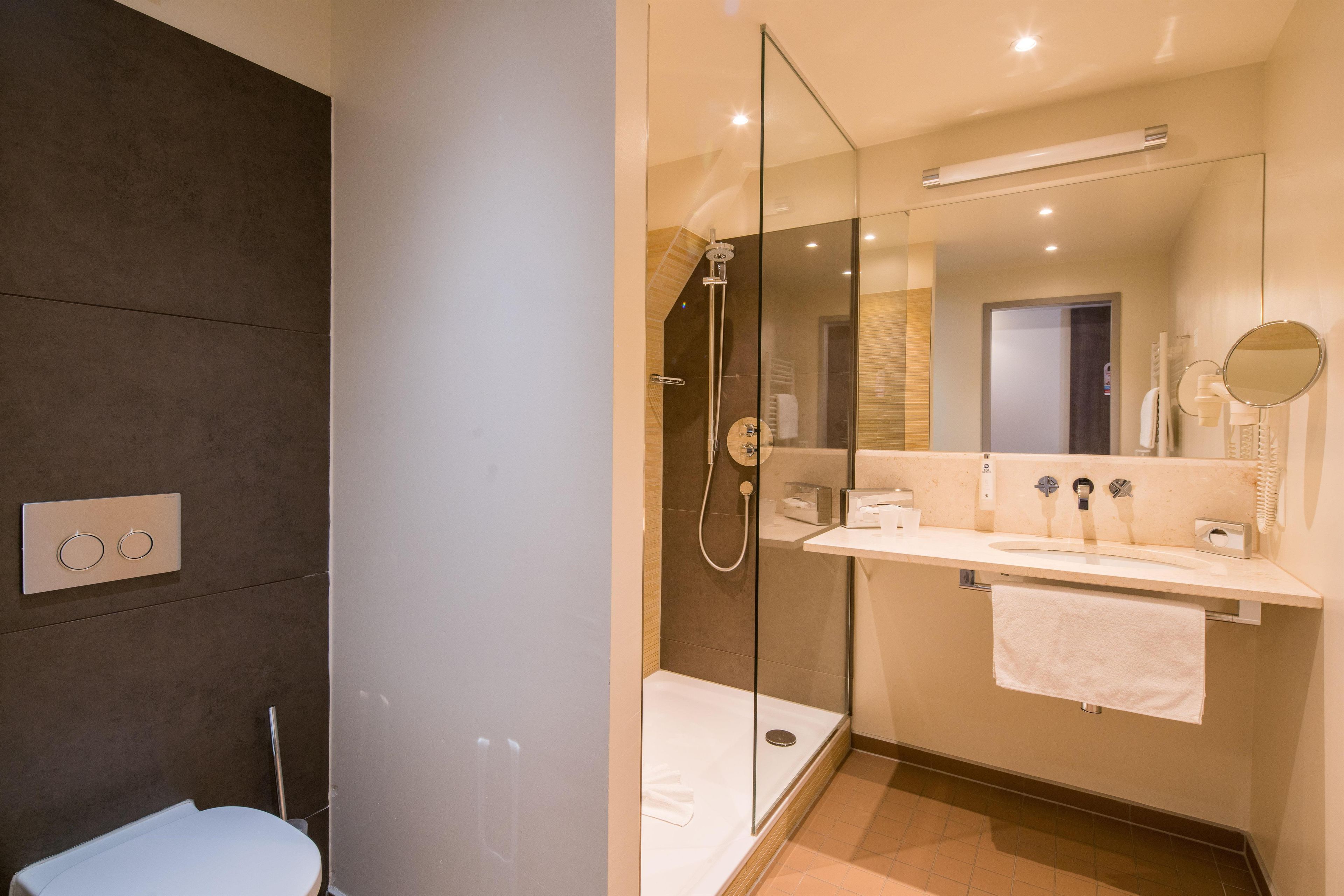 Un baño moderno con ducha envuelta en vidrio, inodoro blanco y tocador con espejo.