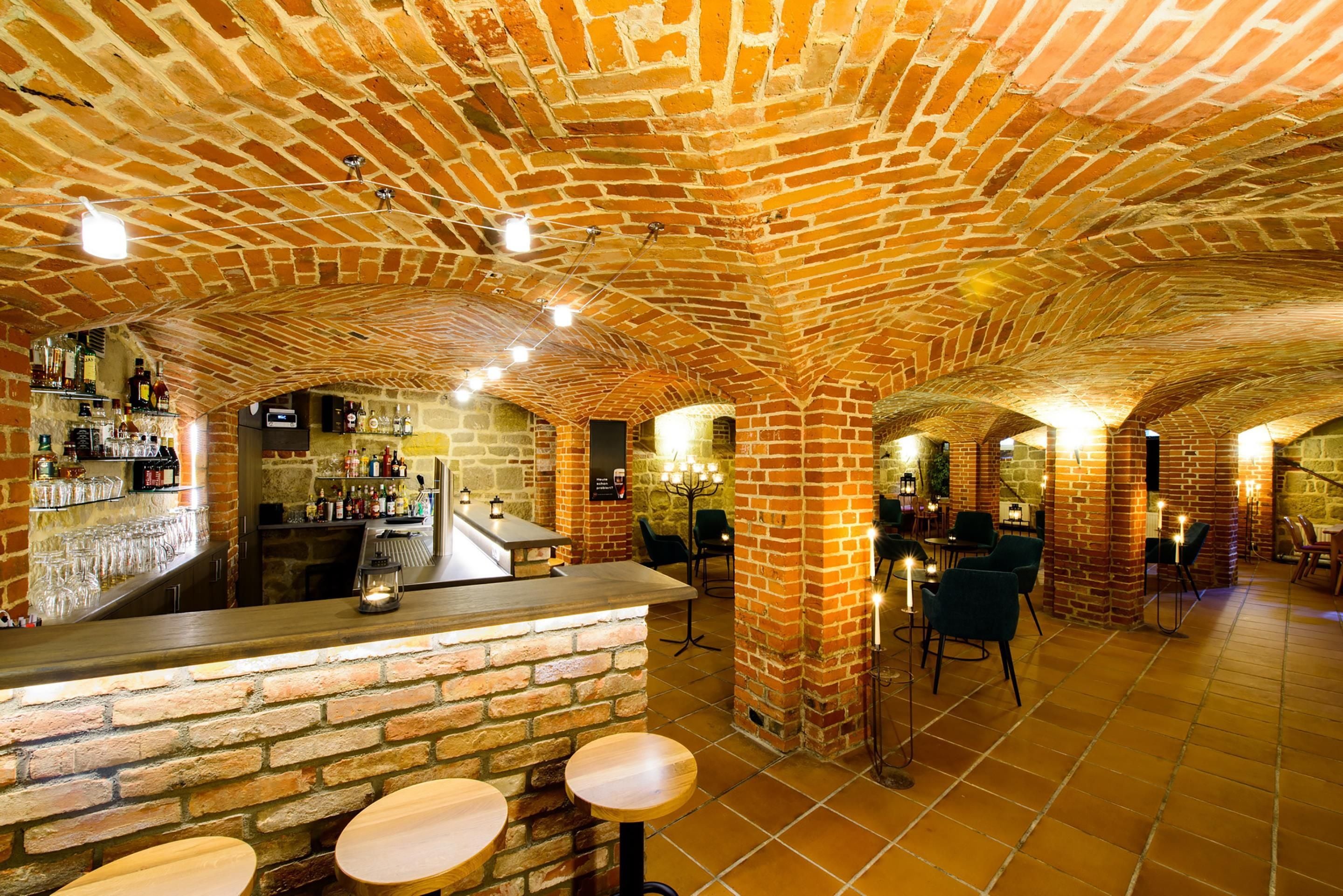 A brick-walled bar area with stools and a counter, surrounded by stone walls and recessed lighting.